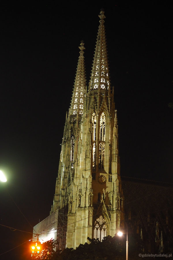 Oświetlone neogotyckie wieże Votivkirche wyciągają nad na spacer.
